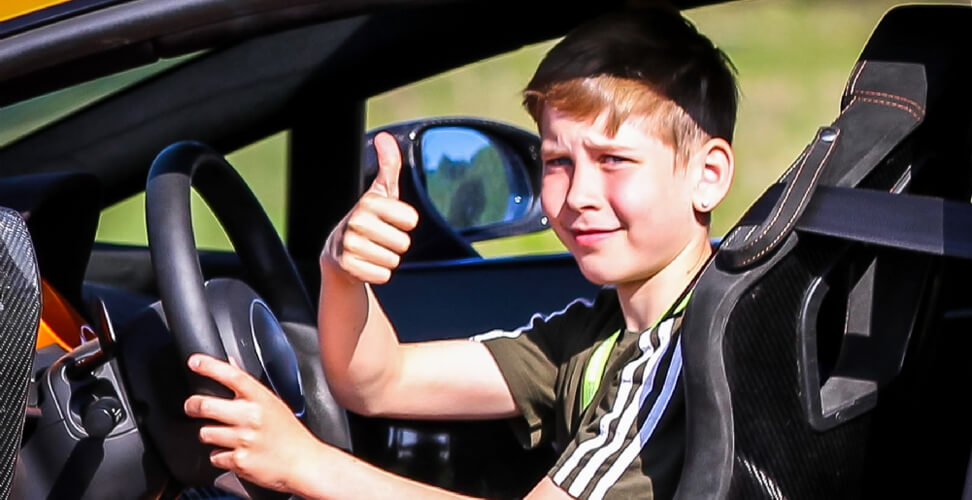 Junior movie driving experience &ndash; boy in driver&rsquo;s seat giving thumbs up, fun kids&rsquo; car adventure activity