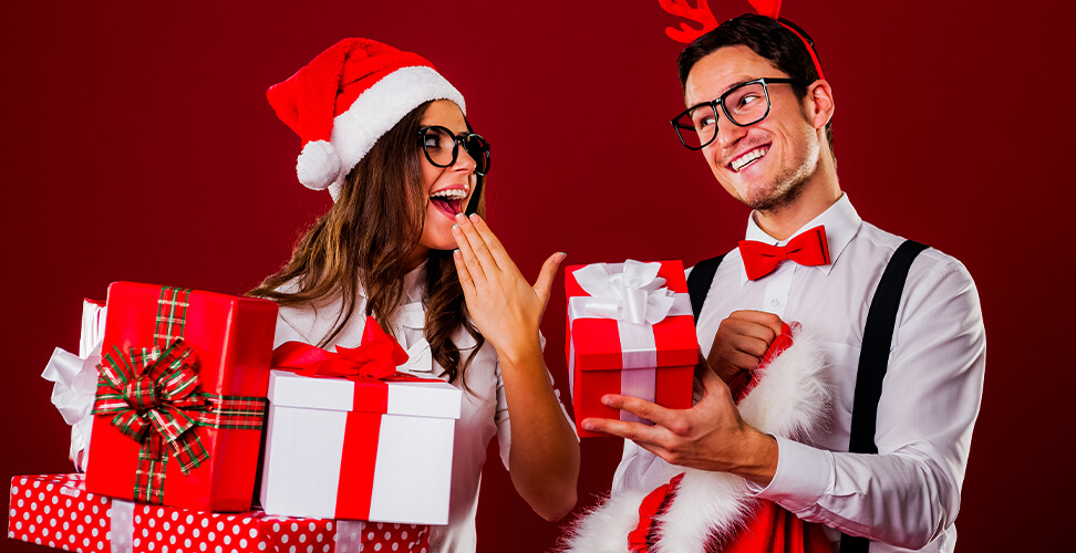Two colleagues wearing glasses and Santa hats exchanging Secret Santa gifts &ndash; office holiday celebration, festive Christmas party, and gift exchange at work
