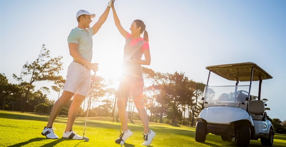 Male and female golfers on the green giving a high five with golf buggy in the background, celebrating a successful game