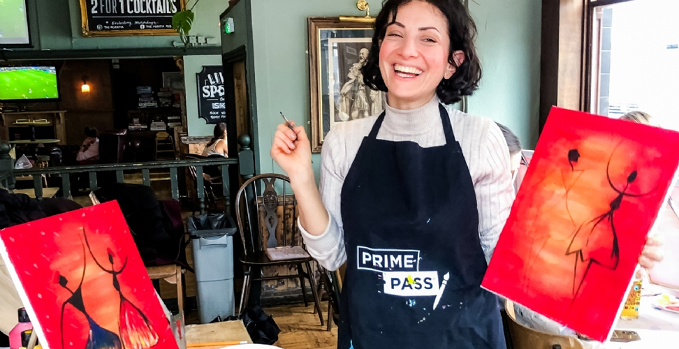 Woman enjoying sip and paint experience, proudly holding up her artwork at creative workshop
