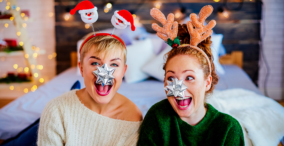 Two women wearing Christmas headbands with star bows on noses laughing and having festive holiday fun
