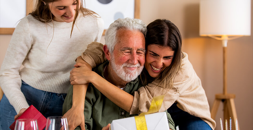 Two granddaughters hugging their grandad while giving him a gift, heartwarming family moment and personalised present idea
