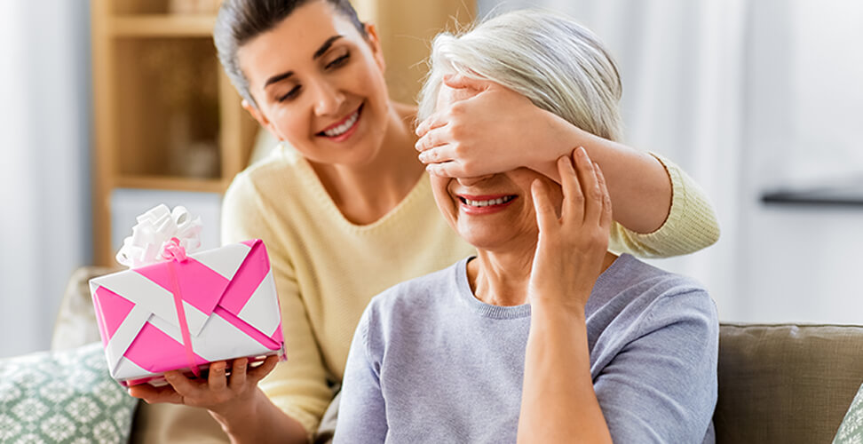 Granddaughter surprising grandma with a gift while covering her eyes, happy family moment and personalised present idea