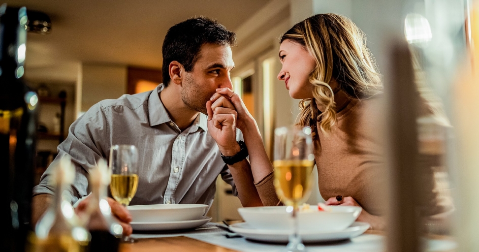 A man tenderly kisses a woman's hand across a dining table during a romantic dinner.