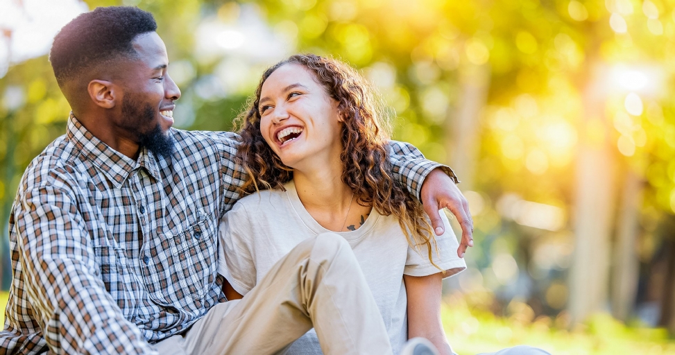Joyful Black man and woman with curly hair embracing and laughing in a sunlit park.