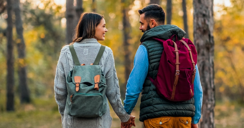 A happy couple holding hands while walking in an autumn forest, looking at each other.