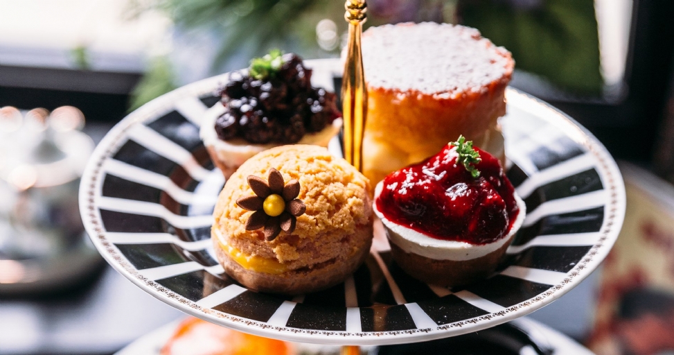 A close-up of an afternoon tea stand featuring four delightful pastries on a black and white striped plate.