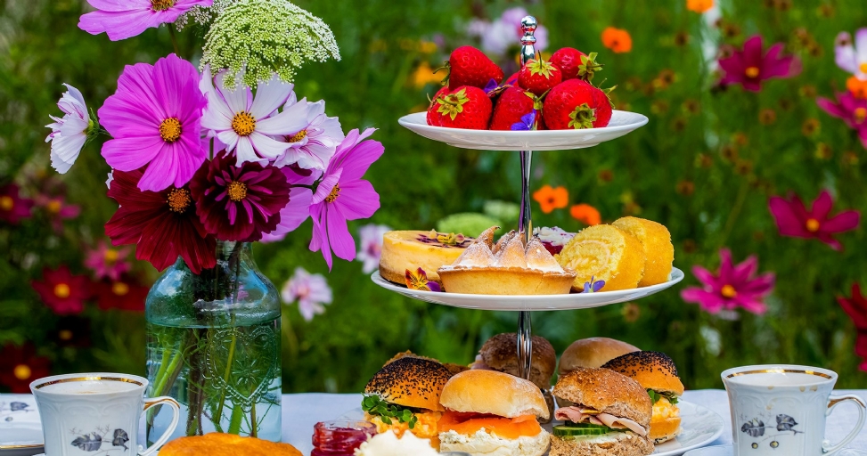 An elegant outdoor afternoon tea in a vibrant garden with a three-tiered stand of treats.