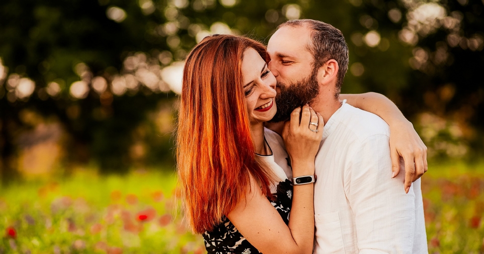 A loving couple shares a tender moment, man kissing woman's cheek in a vibrant outdoor setting.