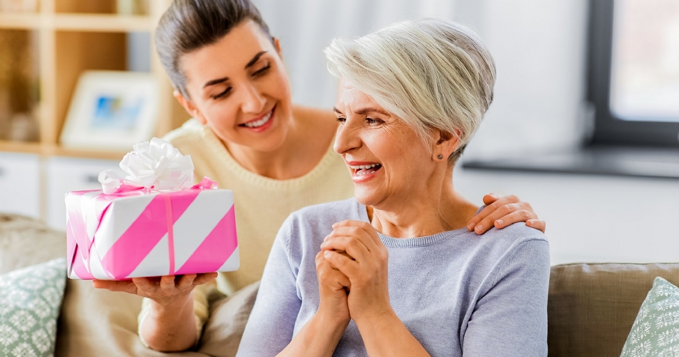 A young woman gives a pink and white striped gift to an older, joyful woman.