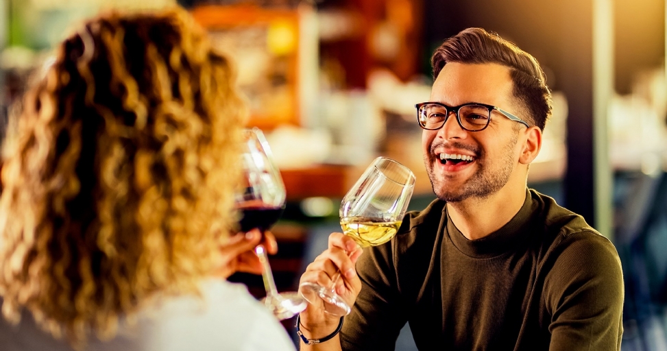 A smiling man in glasses toasts with a woman, holding a glass of white wine.
