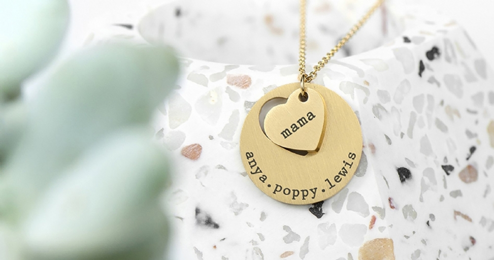 A gold necklace featuring a heart charm with 'mama' and a round charm with 'anya', 'poppy', 'lewis' engraved.