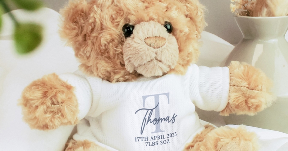 A fluffy brown teddy bear wears a white personalized t-shirt with 'Thomas', a birth date, and weight.
