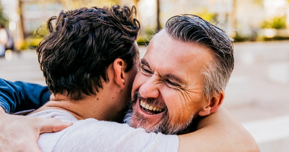 Two men sharing a warm hug, one laughing with joy and eyes closed.