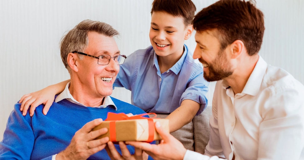 Three generations of men smiling as a father and son present a gift to the grandfather.
