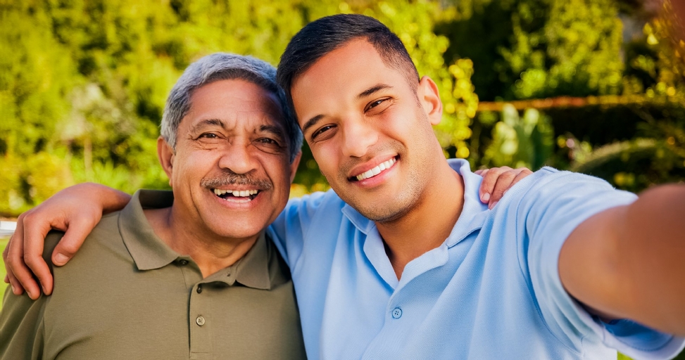 A happy father and son smiling and embracing while taking a selfie outdoors.