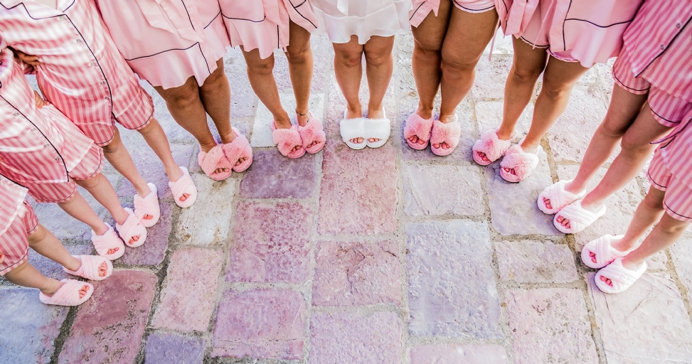 Women in pink striped pajamas and fluffy slippers, with one pair of white slippers, on a stone pavement.