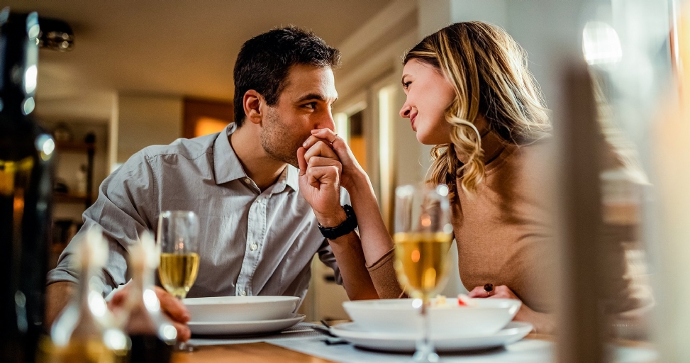 A man tenderly kisses his partner's hand across a dining table during a romantic dinner.