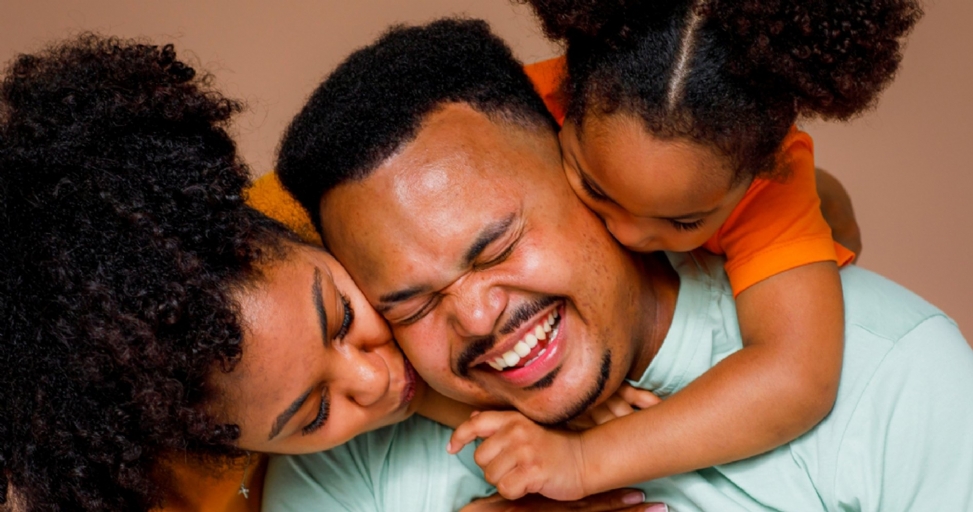 A happy family embracing, with a father laughing between his wife and child.