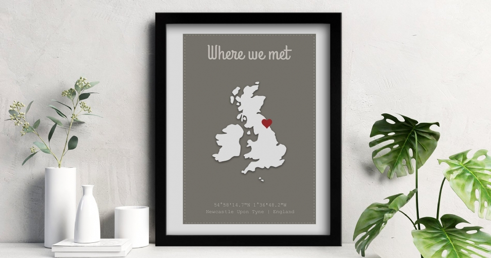 A framed print displaying a map of the UK with a red heart over Newcastle, flanked by plants.
