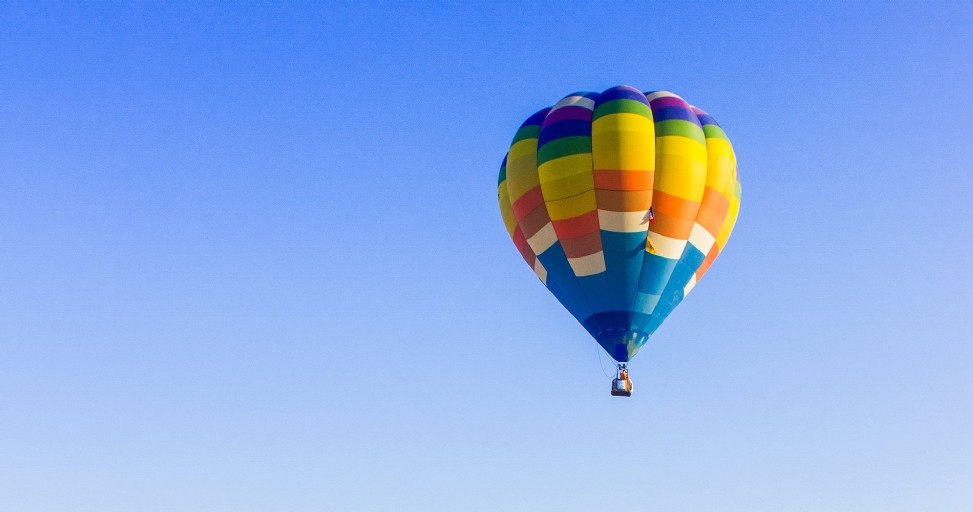A vibrant multi-colored hot air balloon floats gracefully against a clear, expansive blue sky.