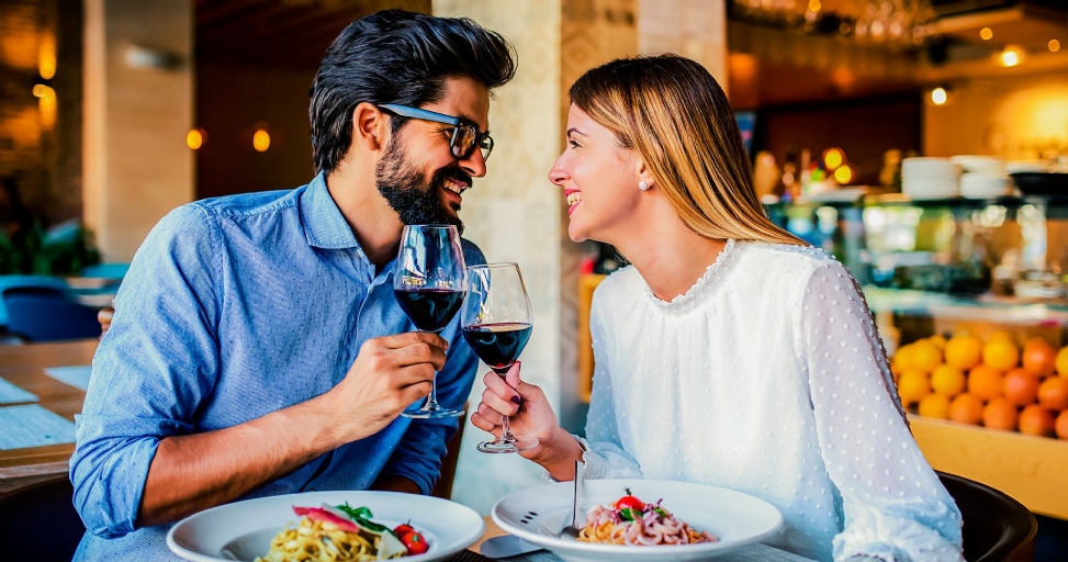 A smiling couple clinking wine glasses during a romantic dinner date in a restaurant.