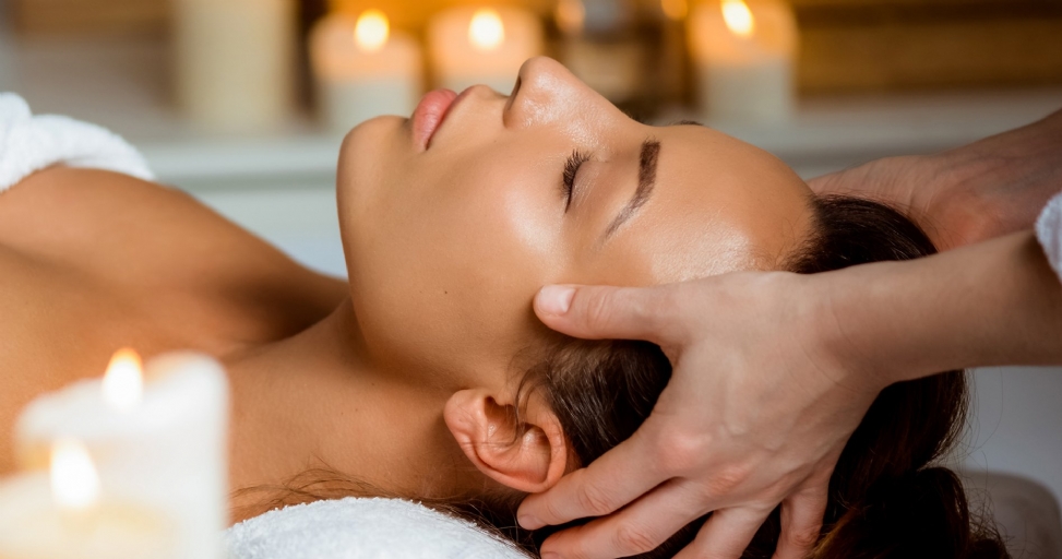 A woman receives a relaxing head massage at a spa, with soft candlelight in the background.