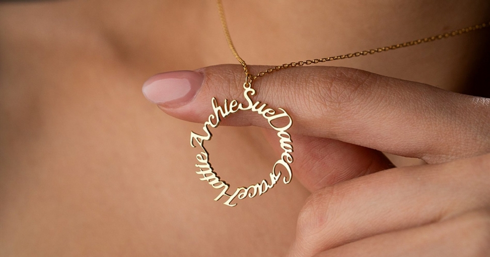 A close-up of a person holding a gold personalized name necklace with several names written on it.