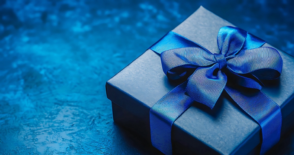 A dark blue gift box with a shiny blue ribbon and bow on a textured blue background.