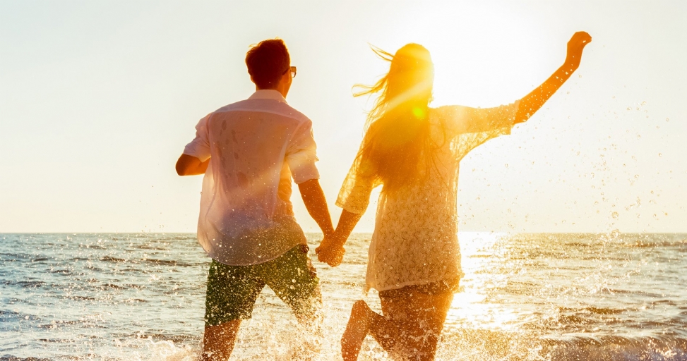 A joyful couple runs hand-in-hand through the sparkling ocean water at sunset.