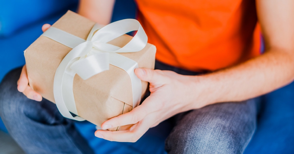 A person holds a thoughtful gift wrapped in simple brown paper tied with a white satin ribbon.