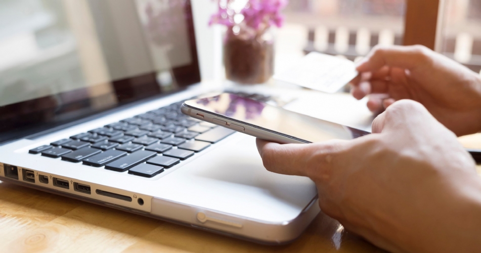 Person using a smartphone and laptop for online shopping with a credit card.