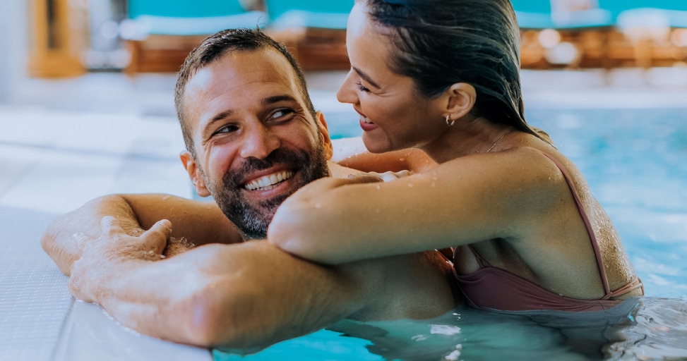 A happy couple smiling and embracing in a swimming pool, enjoying a romantic moment.