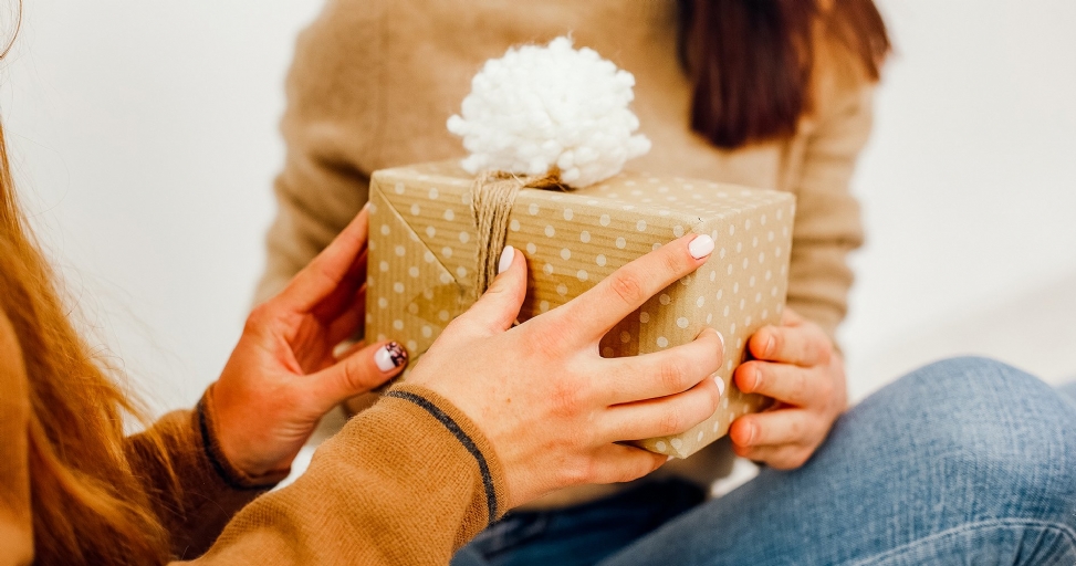 Close-up of two people's hands exchanging a gift box wrapped in polka-dot paper with a white pom-pom.