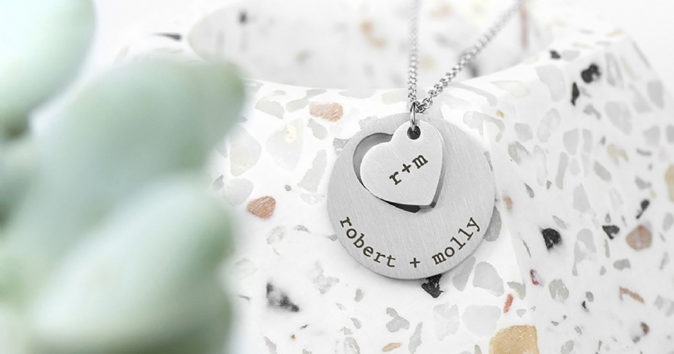 Close-up of a personalized silver necklace with 'r+m' heart and 'robert + molly' round pendants.
