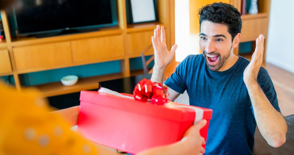 A happy man with raised hands receives a red gift box from another person.