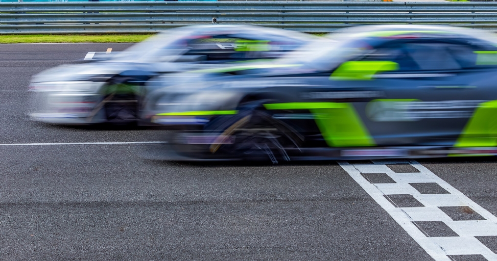 Two race cars in motion, blurred for speed, passing a checkered finish line on a track.