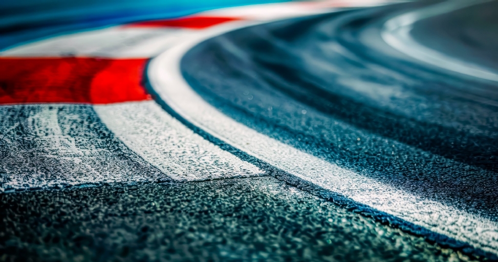 Dynamic close-up of a wet race track corner with vibrant red and white painted lines on asphalt.