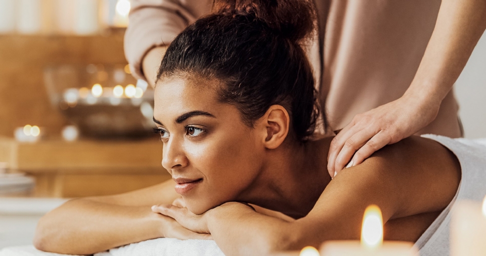 A woman with her hair in a bun enjoys a relaxing back massage in a peaceful spa setting with candles.