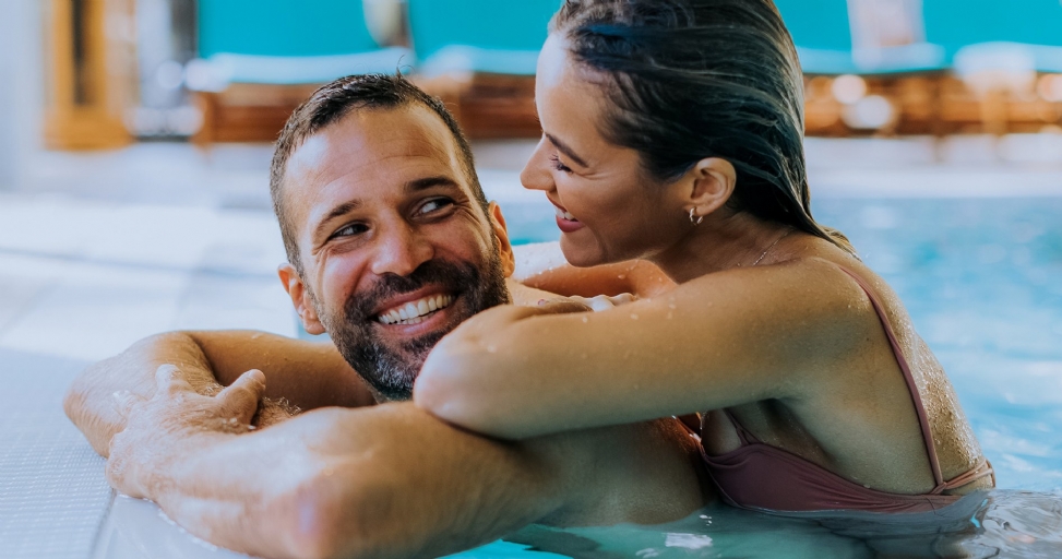 A happy couple smiling and embracing each other while relaxing in a swimming pool.