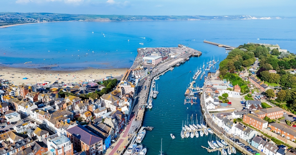 Aerial view of a bustling coastal town with a sandy beach, harbor, and numerous boats.
