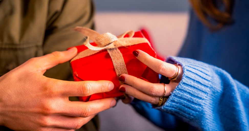 Close-up of two people exchanging a red gift box tied with a rustic ribbon.