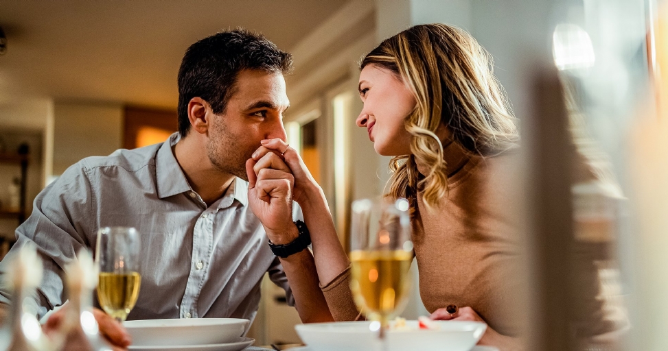 Man lovingly kisses woman's hand across the table during a romantic date.