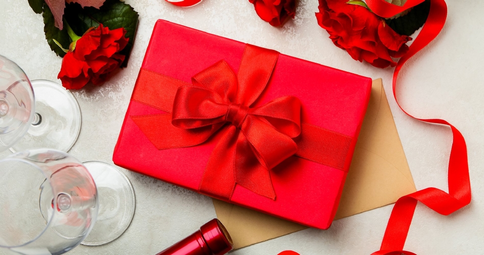 Overhead view of a red gift box with bow, roses, wine glasses, and a bottle.