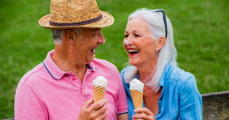 Joyful senior couple sharing ice cream cones outdoors, both with ice cream on their noses.