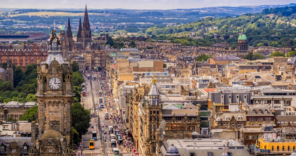 A high-angle panoramic view of Edinburgh, Scotland, featuring a prominent clock tower and a bustling Princes Street.