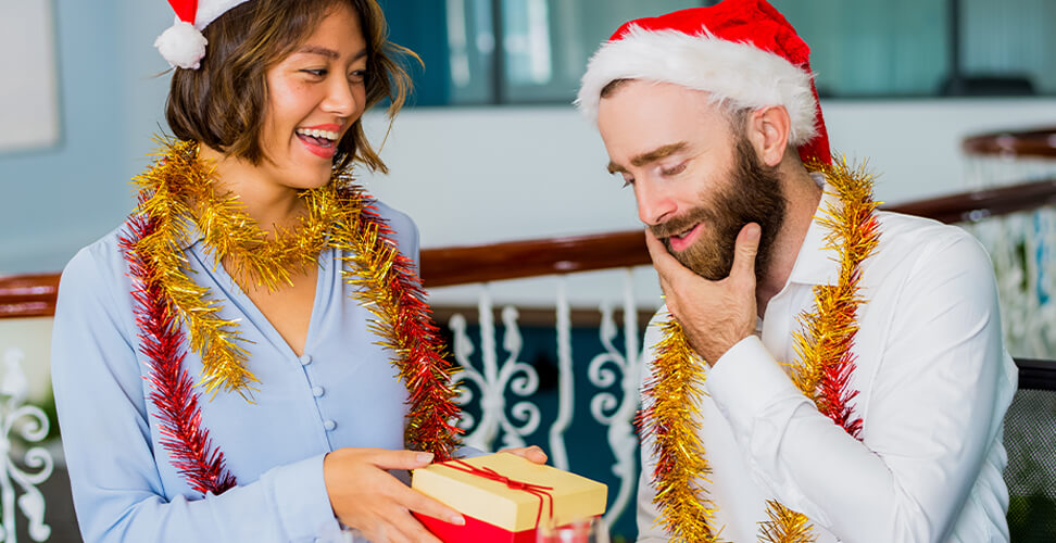 Coworkers in Santa hats exchanging Secret Santa gifts with tinsel &ndash; festive office holiday party celebration