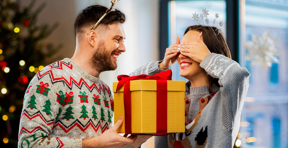 Colleagues in festive Christmas jumpers exchanging Secret Santa gifts &ndash; fun office holiday party celebration
