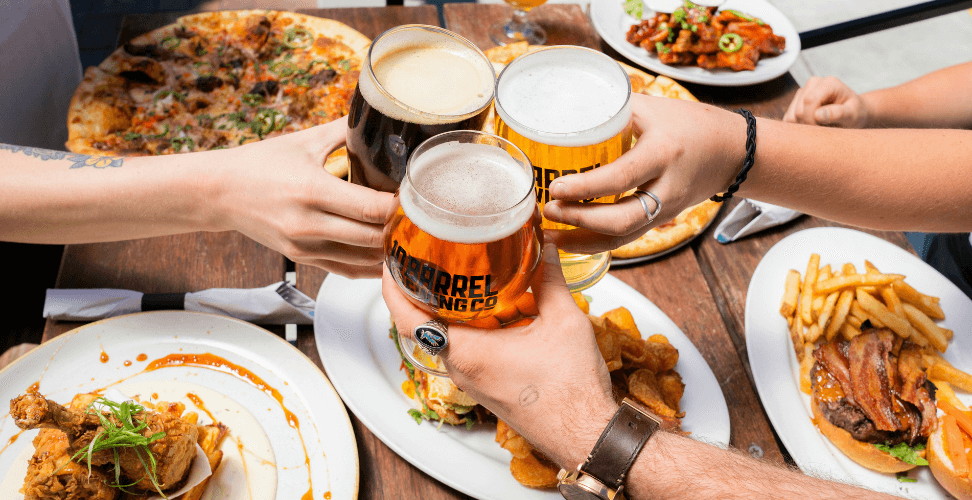 A group of people holding glasses of beer and food on a table