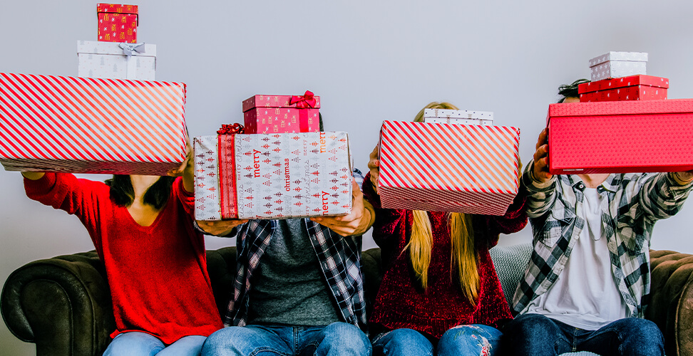 Four friends holding out Christmas gifts to the camera during White Elephant gift exchange